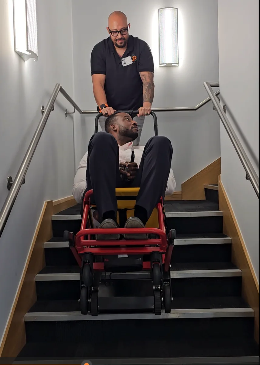 An operator bringing a seated man down a stairwell in an evacuation chair
